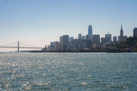 Photo for Daytime view of San Francisco skyline across the glistening bay with iconic Transamerica Pyramid, Salesforce Tower, and part of Golden Gate Bridge under a clear blue sky. - Royalty Free Image