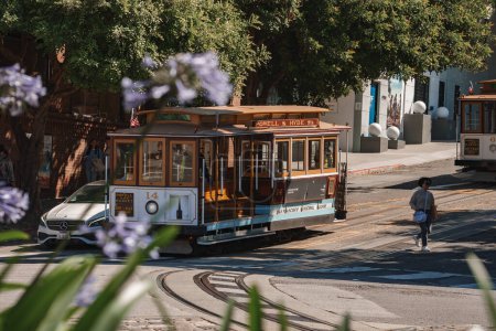 Photo for Classic San Francisco cable car, Powell and Hyde route, symbol of city charm. Blurred flowers, pedestrian, urban scene with historic transportation. Sunny day, iconic area. - Royalty Free Image