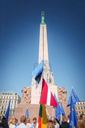 Téléchargez les photos : Un rassemblement animé près du monument de la liberté à Riga, en Lettonie, marque le vingtième anniversaire de son adhésion à l'UE. Les drapeaux européens ajoutent de la couleur à la célébration dans le cadre historique de la vieille ville. - en image libre de droit