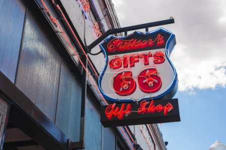 Photo for Vibrant retro style neon sign, Cruisers Gifts 66 Gift Shop, in red and blue with white accents against cloudy sky. Likely in Williams near Grand Canyon. - Royalty Free Image