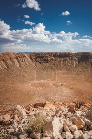 Impressive view of Meteor Crater, Barringer Crater in Arizona, USA. Vast, circular meteorite impact site with rocky terrain, clear blue sky, and sunlit crater walls.