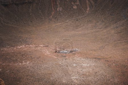 Karge Landschaft Arizonas am Meteor Crater, einem geologischen Wunder, das durch einen Meteoriteneinschlag entstanden ist. Gedämpfte Erdtöne, zerklüftete Wände und felsiges Becken schaffen eine drastische Szene.