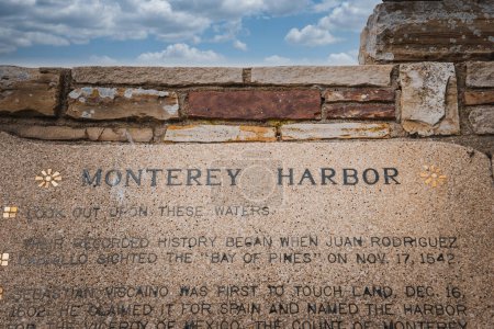 Gedenktafel in Ziegelmauer mit der Aufschrift MONTEREY HARBOR. Text beschreibt historische Ereignisse aus dem Jahr 1542. Standort wahrscheinlich in der Nähe des Hafens von Monterey, unter bewölktem Himmel.
