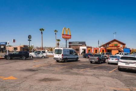 Photo for Busy parking lot in Barstow, USA along Route 66. McDonalds with golden arches in background. Modern design, palm trees, clear sky, other signs nearby. - Royalty Free Image