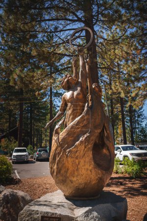 Téléchargez les photos : Sculpture en bronze de figure féminine atteignant un objet circulaire à l'extérieur, avec des cheveux et des vêtements qui coulent, arbres en arrière-plan à Tahoe, Californie. - en image libre de droit