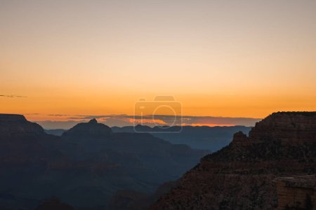 Serene sunset view over a rugged canyon landscape with warm orange hues fading into blue skies. Reminiscent of Grand Canyon, Arizona, USA. Peaceful and contemplative.