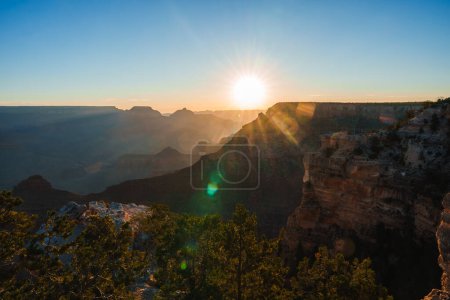 Atemberaubender Blick auf eine Schlucht bei Sonnenaufgang oder Sonnenuntergang. Die Sonne wirft warmes Licht auf zerklüftetes Gelände, klaren Himmel, Schichten von Felsformationen. Silhouettierte Felsvorsprünge, weiträumiger Blick im Grand Canyon, USA.