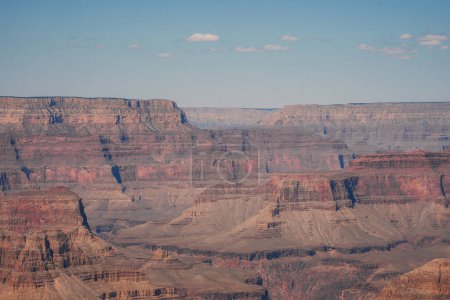 Une vue imprenable sur le Grand Canyon en Arizona, États-Unis. Couches de formations rocheuses rouges et brunes, sculptées par le fleuve Colorado, sous un ciel bleu clair.