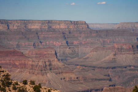 Découvrez la beauté majestueuse du Grand Canyon en Arizona, aux États-Unis. La photographie montre de superbes couches de formations rocheuses rouges, brunes et grises sous un ciel bleu clair.