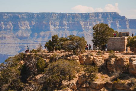Photo for Scenic view of Grand Canyon with vast landscape, rock formations, visitors enjoying overlook, small structure, sparse vegetation, layered cliffs under blue sky. - Royalty Free Image