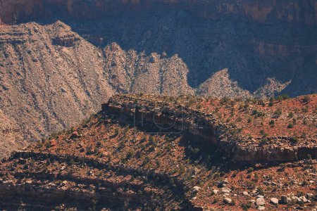 Explorez un paysage accidenté et étendu avec des formations rocheuses stratifiées dans des tons de rouge, de brun et de gris. Réminiscence des paysages désertiques du Grand Canyon ou du Sud-Ouest américain.