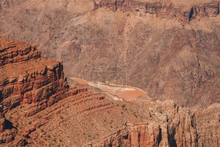 Discover the majestic beauty of a rugged landscape with layered rock formations and a winding river cutting through steep canyon walls at the Grand Canyon.