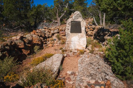 Historische Markierung auf einem großen Steinsockel in natürlicher Umgebung, umgeben von Felsen und Bäumen am Grand Canyon. Gedenktafel-Inschrift nicht lesbar.