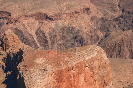Dramatic canyon landscape with red, orange, and brown sedimentary rock formations. Arid terrain devoid of vegetation, resembling the Grand Canyon. Morning or late afternoon lighting.