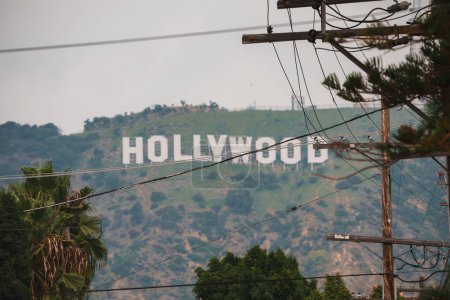Téléchargez les photos : Iconic Hollywood Signe en vue lointaine contre les collines, partiellement obscurci par les lignes électriques. Cadre urbain à Los Angeles, Californie. Atmosphère folle. - en image libre de droit
