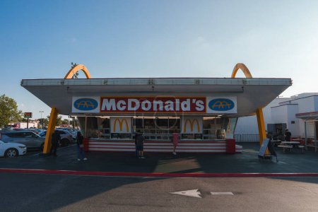 Photo for Iconic McDonalds restaurant featuring retro design with golden arches and red white color scheme. Clear sky and cars parked. Location may be in Los Angeles. - Royalty Free Image