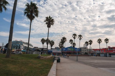 Photo for Explore a serene scene along a wide walkway in Venice Beach, Los Angeles. Palm trees, beachfront businesses, and a vibrant sky create a relaxed atmosphere. - Royalty Free Image