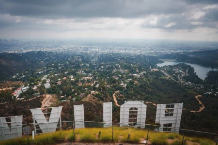 Photo for Iconic Hollywood Sign overlooking Los Angeles skyline from elevated position in hills. Overcast sky, cityscape, greenery, reservoir visible. Urban and natural blend captured. - Royalty Free Image