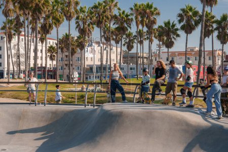 Photo for Vibrant scene at bustling skatepark in Venice Beach, Los Angeles. Diverse group skateboarding in sunny weather, surrounded by palm trees and urban backdrop. - Royalty Free Image