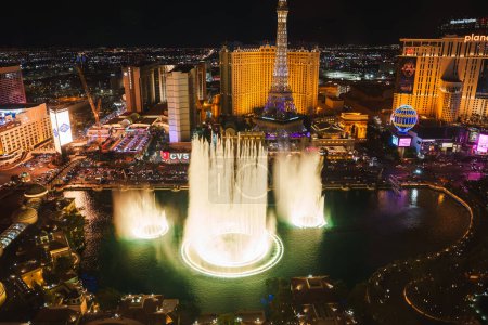 Photo for Vibrant night scene of Las Vegas Strip with spectacular fountain show, lit jets of water, iconic hotels, Eiffel Tower replica, and bustling energy. Aerial view captures dynamic atmosphere. - Royalty Free Image