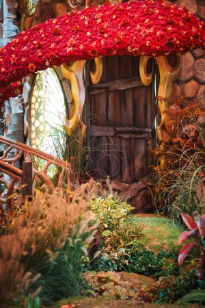 Photo for Whimsical fairy tale scene with charming wooden door in a stone wall, under a mushroom canopy adorned with vibrant red flowers, possibly in Las Vegas. - Royalty Free Image