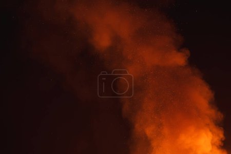 Dynamic scene of large fire at night in a desert setting. Bright orange flames contrast with dark smoke, creating a striking visual display in the dark sky.