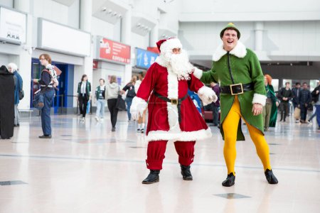Foto de BIRMINGHAM NEC, Reino Unido - 13 de noviembre de 2022. Un par de cosplayers masculinos vestidos como Buddy The Elf y Santa Claus en MCM Birmingham Comic Con 2022 - Imagen libre de derechos
