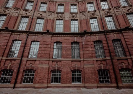 Téléchargez les photos : Vue grand angle plein cadre d'un imposant bâtiment d'usine victorien avec brique rouge et rangées de cadres de fenêtre ornés et architrave avec espace de copie - en image libre de droit