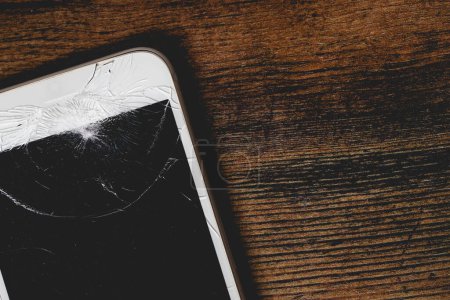 Photo for A close up of a damaged mobile phone with cracked screen for repair on a wooden background with copy space - Royalty Free Image