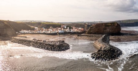 Téléchargez les photos : Une vue aérienne du pittoresque village de pêcheurs du Yorkshire de Staithes qui est une destination touristique populaire dans le nord-est de l'Angleterre avec brise-lames artificiels - en image libre de droit