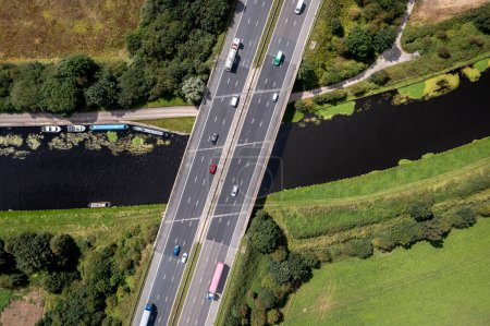 Foto de Vista aérea directamente encima de una concurrida autopista del Reino Unido que pasa por un puente de río o canal en el campo - Imagen libre de derechos