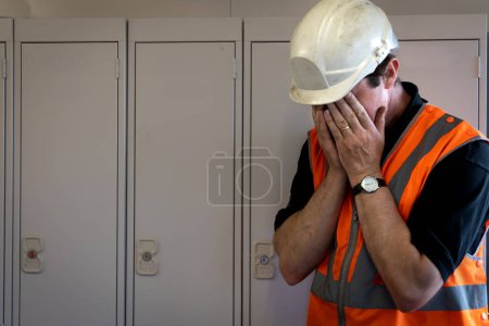 Ein männlicher Angestellter mit dem Kopf in den Händen, der verzweifelt darum kämpft, bei der Arbeit in einem Industrie- oder Bauumfeld in einem Konzept für psychische Gesundheit zurechtzukommen