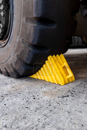 Photo for A yellow heavy duty wheel chock wedged against a vehicle tyre as a safety measure to prevent the vehicle from rolling away with copy space - Royalty Free Image