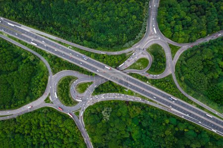 Photo for Aerial landscape view directly above a busy motorway junction cutting a swathe through dense woodland with green tree canopy providing carbon capture from exhaust fumes in an environmental concept - Royalty Free Image