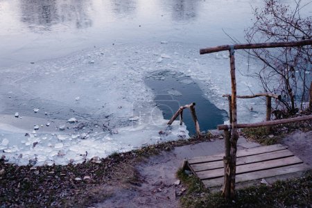 Lugar de baño de hielo en el río con escalones y rieles de madera. Lago nevado frío o vista al río. Paisaje invierno.