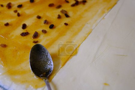 Foto de Testo crudo de levadura dulce en una bandeja para hornear con cuchara, relleno con pasas y mermelada de naranja. Preparación para hornear. El concepto de cocineros y hornear - Imagen libre de derechos