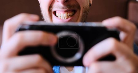 Young man passionately engages with handheld game console, vividly expressing victory emotions in a close-up selective focus shot. Ideal for dynamic gaming content.