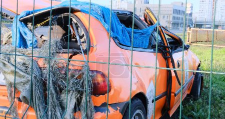 A crashed orange car with a dented body and roof sits abandoned in the grass, depicting the concept of an accident. Perfect for illustrating automotive mishaps and safety awareness.