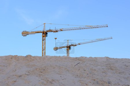 dos grúas de construcción torre sobre un montículo de arena sobre un telón de fondo de cielo azul. Perfecto para ilustrar el progreso de la construcción y el desarrollo industrial.