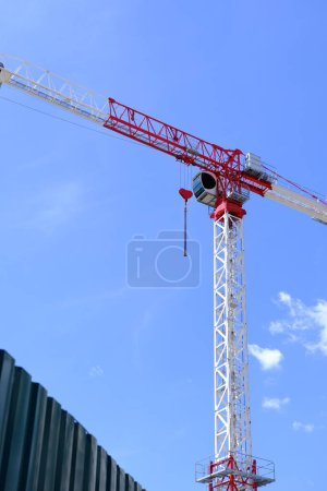 Red and white crane with heart-shaped hook against blue sky. Romantic crane, love-themed equipment, construction site, Valentines Day concept