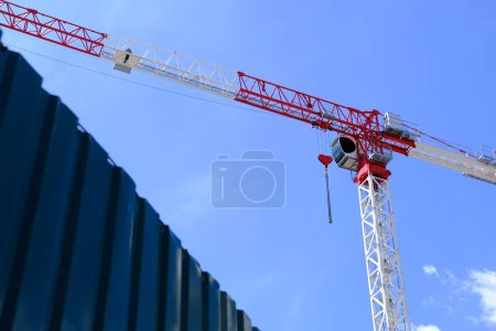 Red and white crane with heart-shaped hook against blue sky. Romantic crane, love-themed equipment, construction site, Valentines Day concept