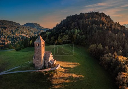 Foto de Hafling, Italia - Vista aérea de la iglesia de montaña de Santa Catalina (Chiesa di Santa Caterina) cerca de Hafling - Avelengo con una cálida puesta de sol de otoño en los Dolomitas italianos en el Tirol del Sur - Imagen libre de derechos