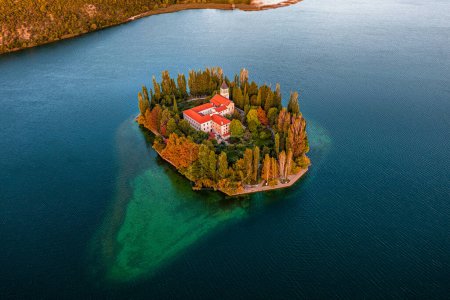 Photo for Visovac, Croatia - Aerial view of the beautiful island Visovac Christian monastery in Krka National Park on a bright autumn morning with warm golden lights at sunrise and blue water - Royalty Free Image