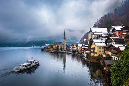 Photo for Hallstatt, Austria - Iconic view of world famous Hallstatt, the Unesco protected lakeside town with Hallstatt Lutheran Church on a cold foggy day with traditional passenger ship and snowy rooftops - Royalty Free Image