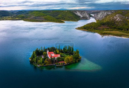Photo for Visovac, Croatia - Aerial panoramic view of Visovac Christian monastery in Krka National Park on a summer morning with the peaks of Kijevski Kozjak and cloudy sky at background - Royalty Free Image