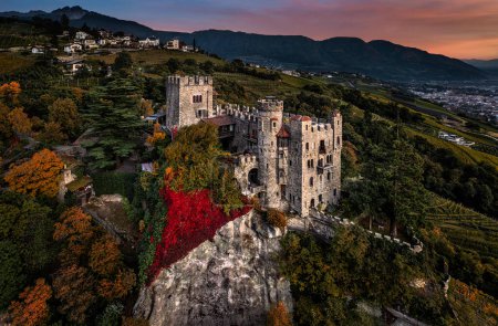 Téléchargez les photos : Merano, Italie - Vue panoramique aérienne du célèbre château Brunnenburg (Castel Tirolo) avec la ville de Merano, les Dolomites italiennes et le coucher de soleil coloré en arrière-plan à l'automne - en image libre de droit