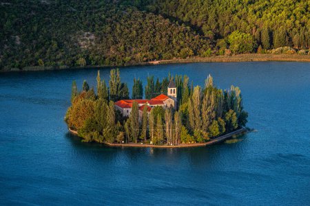Téléchargez les photos : Visovac, Croatie - Monastère chrétien Visovac dans le parc national de Krka par un matin d'été lumineux avec des lumières dorées chaudes au lever du soleil et l'eau bleue - en image libre de droit