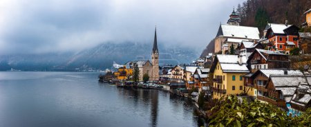 Téléchargez les photos : Hallstatt, Austria - Panoramic view of world famous Hallstatt, the Unesco protected lakeside town with Hallstatt Lutheran Church on a cold foggy day with snowy winter rooftops at Salzkammergut region - en image libre de droit