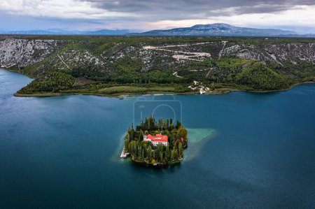 Téléchargez les photos : Visovac, Croatia - Aerial view of Visovac Christian monastery in Krka National Park on a summer morning with the peaks of Kijevski Kozjak and cloudy sky at background - en image libre de droit