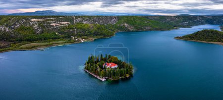 Photo for Visovac, Croatia - Aerial panoramic view of Visovac Christian monastery in Krka National Park on a summer morning with the peaks of Kijevski Kozjak and cloudy sky at background - Royalty Free Image